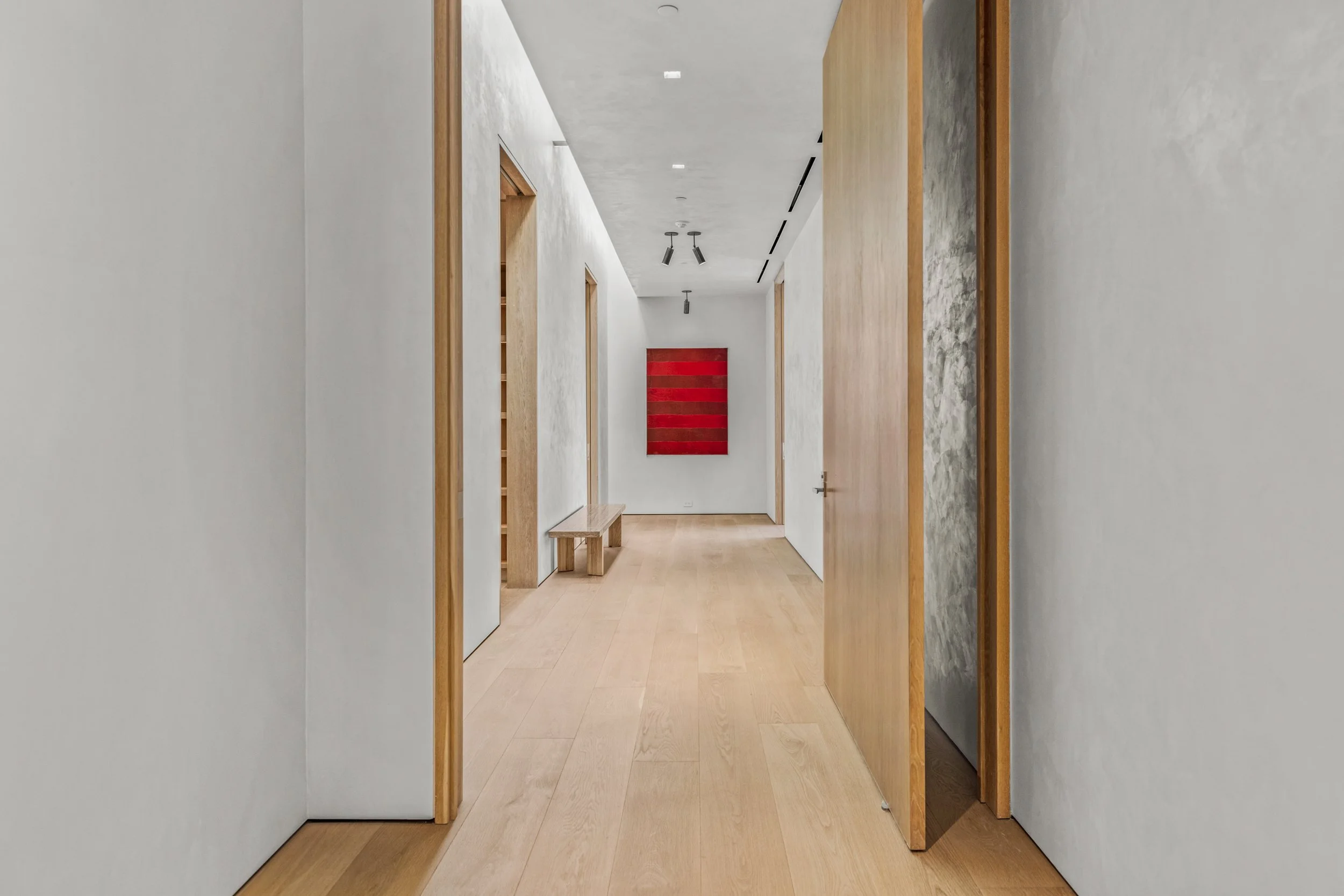 Bright hallway with light wood floors ending at a large red-striped abstract painting.