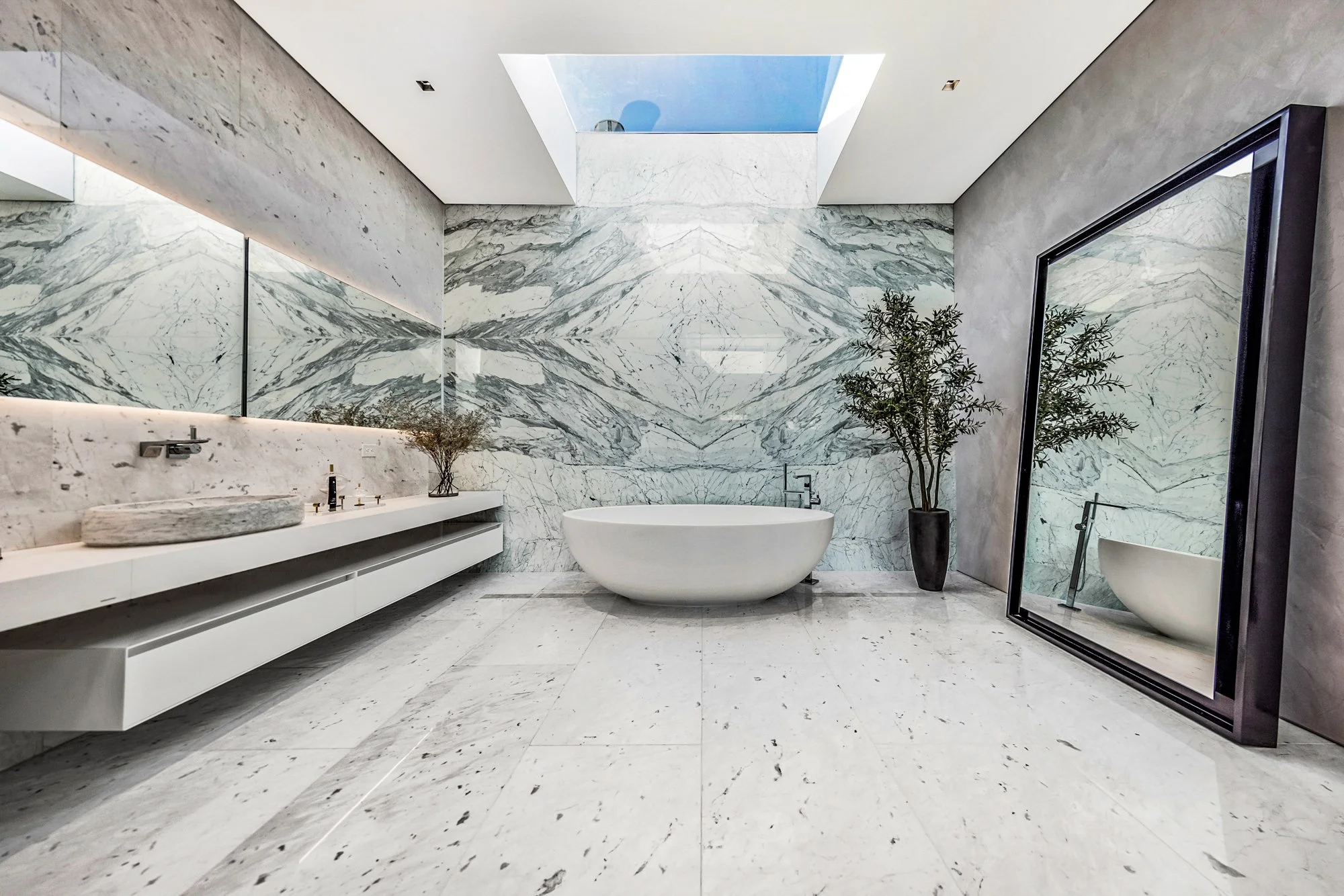 Marble bathroom with a white freestanding tub under a skylight and a floating vanity.