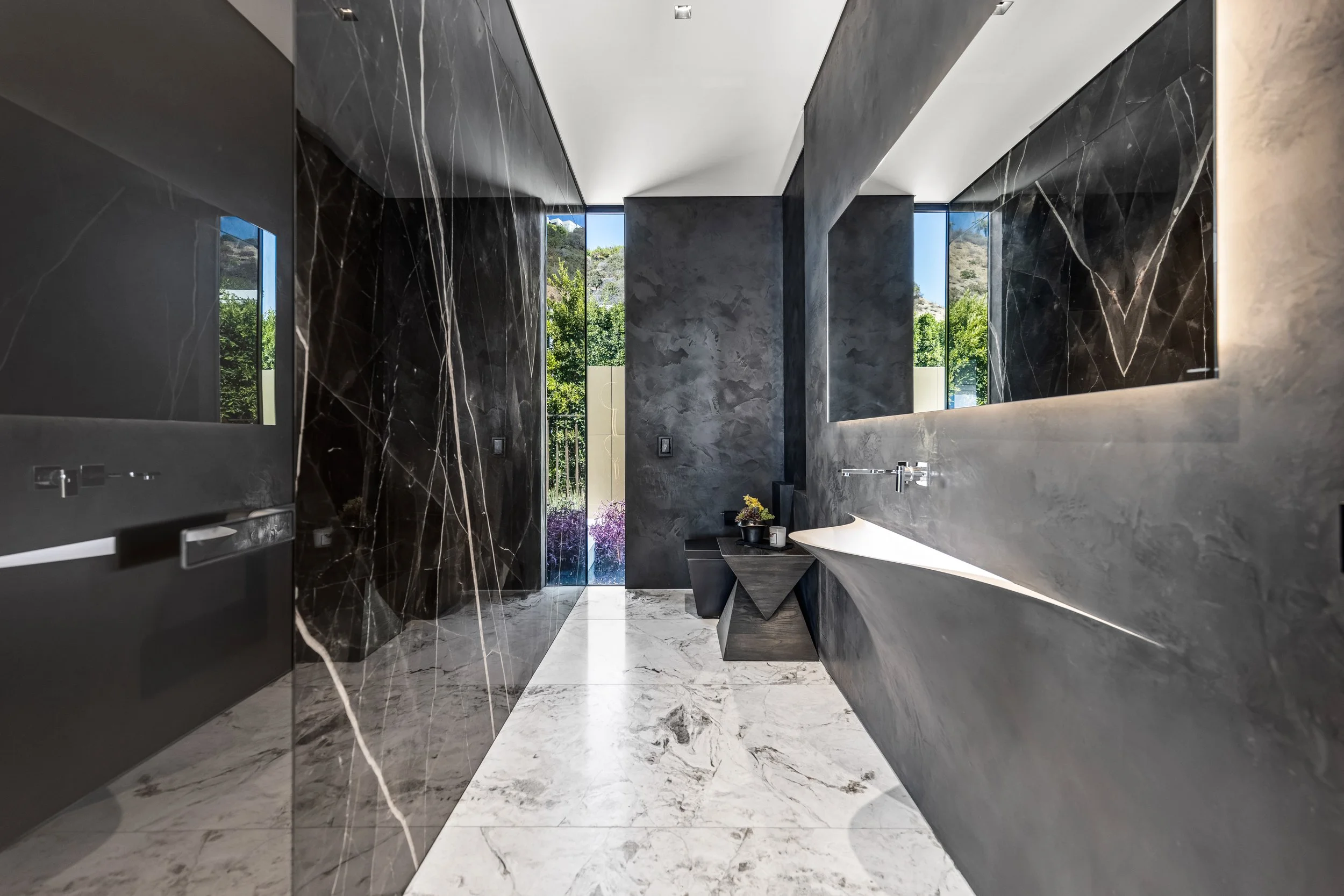 Bathroom with dark textured walls, white marble floors, and a sculptural white sink by a window.