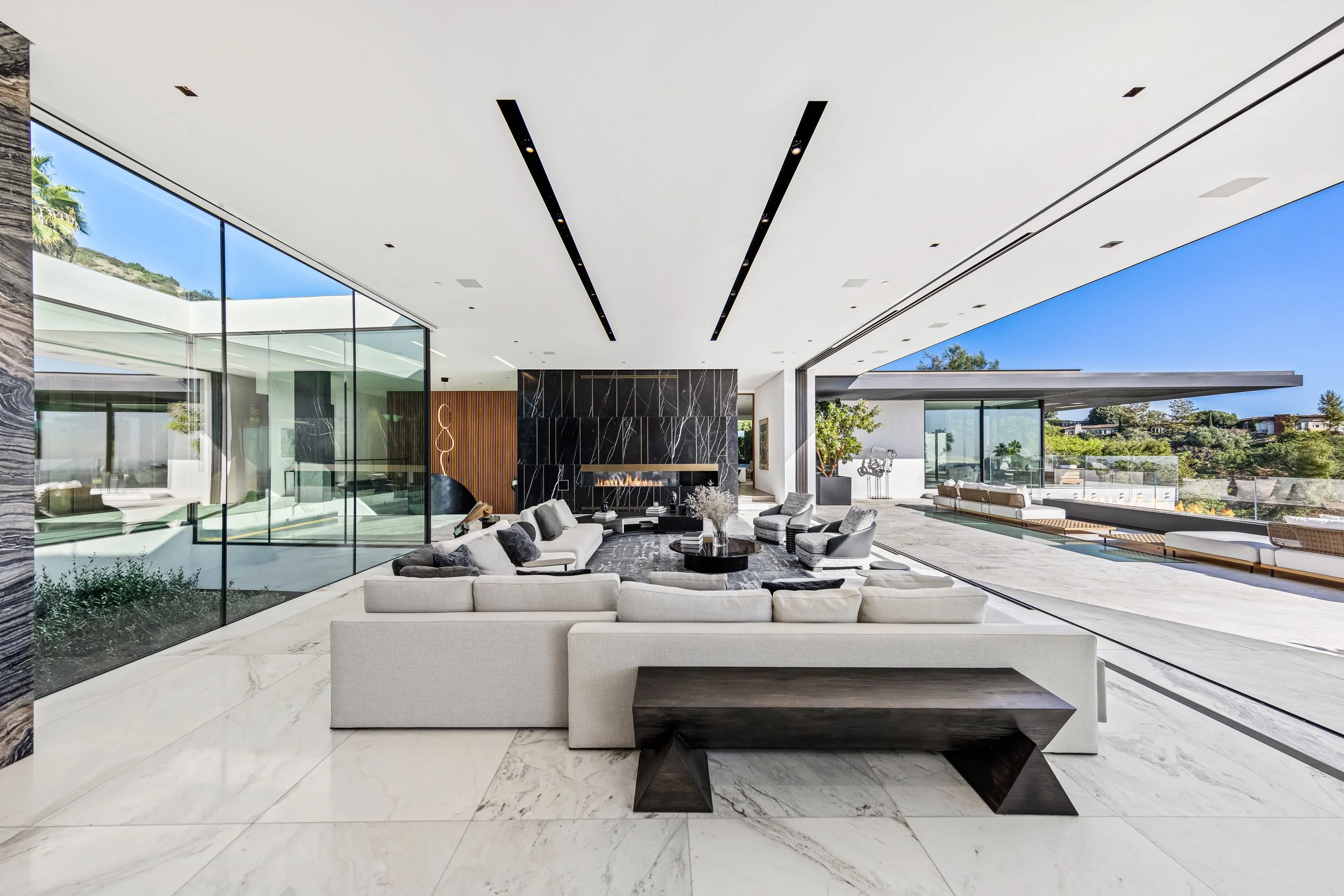 Open living room with white marble floors and a black marble fireplace opening to a sunny terrace.