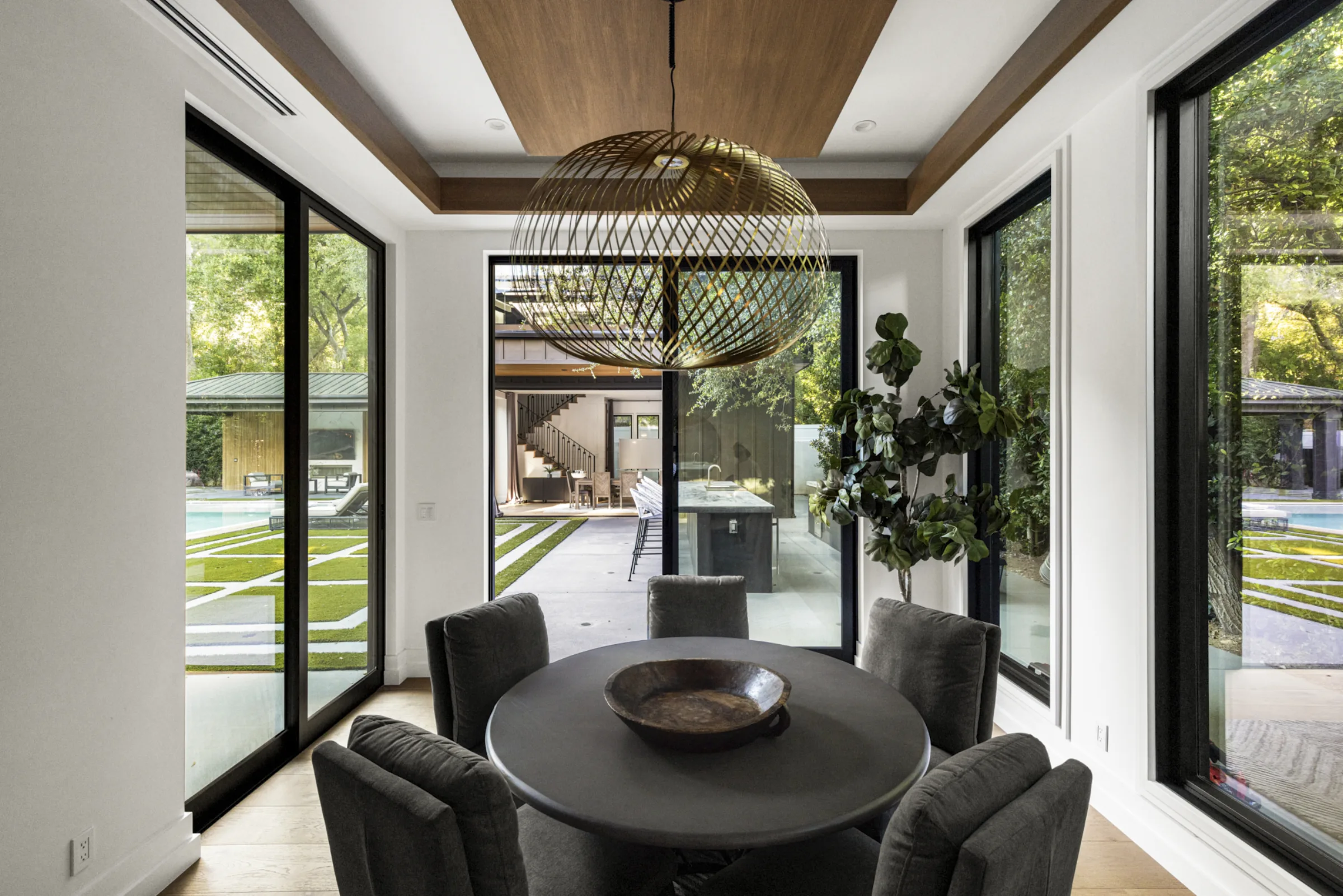 Breakfast nook with a round table and spherical pendant opening to a covered outdoor kitchen and pool.