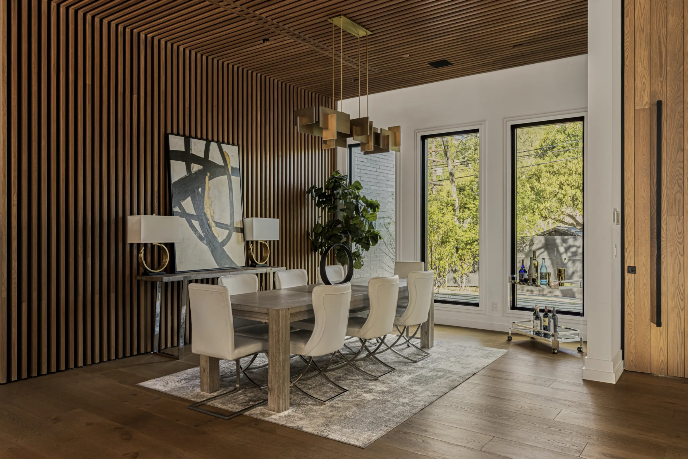 Dining room with a wood-slat ceiling and wall, brass geometric chandelier, and tall garden windows.