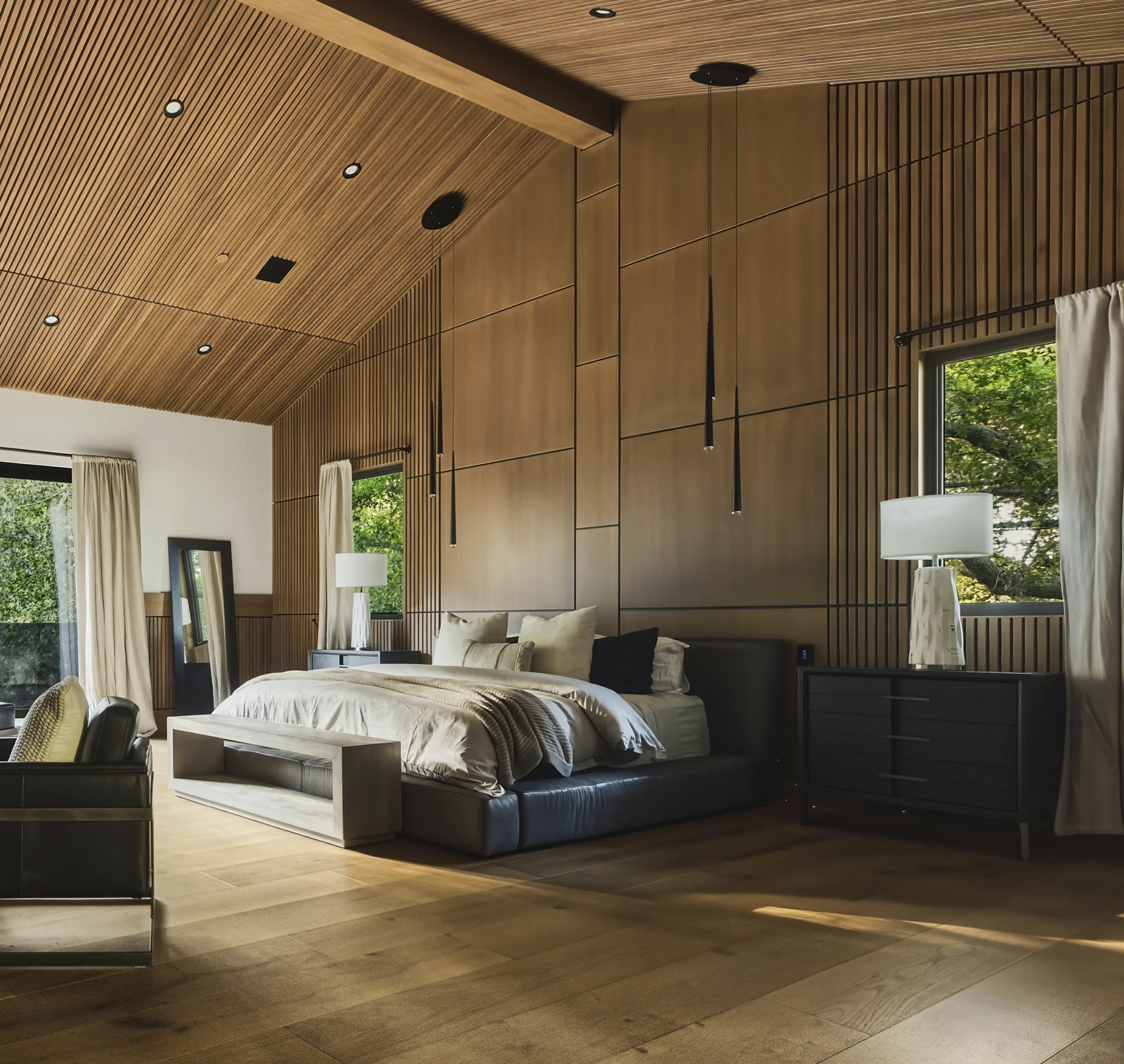 Primary bedroom with a vaulted wood-slat ceiling, dark bed, and needle pendants in soft daylight.